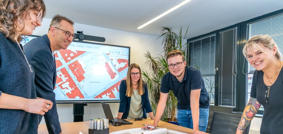 The picture shows a group of people bending over a map lying on a table.