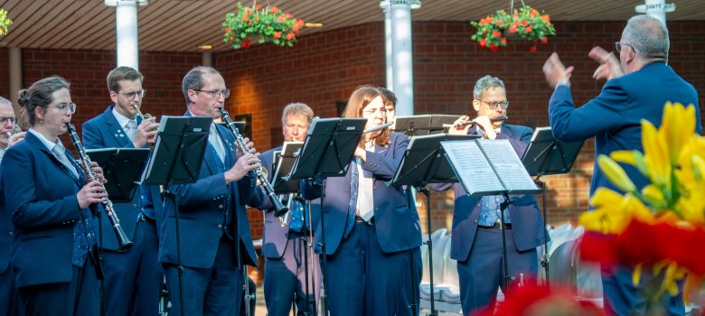 Een dirigent staat voor muzikanten met blaasinstrumenten.