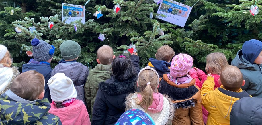 Kinderen staan voor kerstbomen en versieren ze.