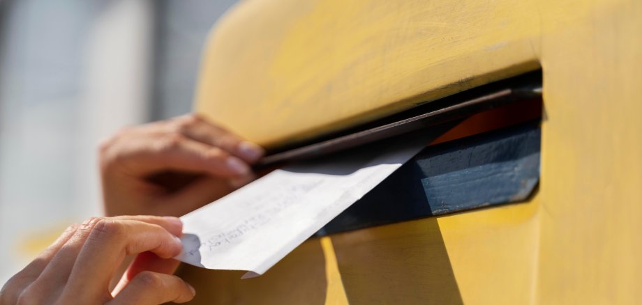 Briefe werden in einen Briefkasten geworfen.